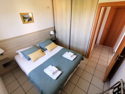 Chambre moderne de la Résidence Saint Michel à L'île Rousse avec lit queen-size, oreillers jaunes, climatisation et porte en bois