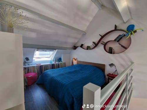 Chambre moderne de l'appartement de Carol à Sauzon, Belle-Île-en-Mer, avec literie rayée bleue, étagères murales courbes et puits de lumière