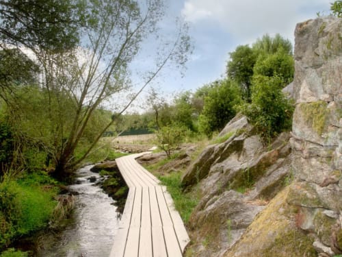 Pasarela de madera sobre arroyo en Cabañas Compostela, Santiago de Compostela, con acantilados rocosos y vegetación exuberante