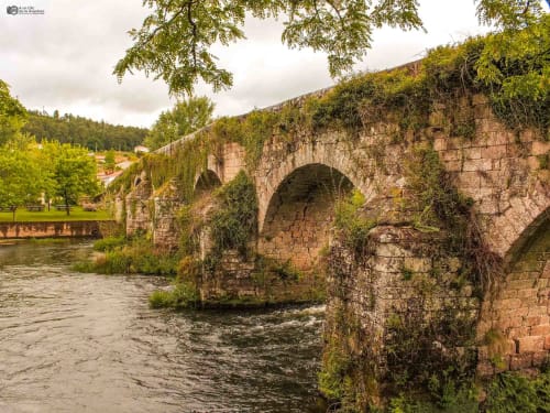 Antiguo puente de piedra con arcos que cruza el río cerca de Cabañas Compostela en Santiago de Compostela, rodeado de exuberante vegetación