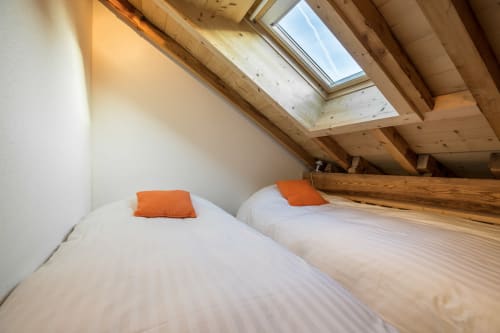 Attic bedroom with two beds, orange pillows, wooden beams, and skylights at Les Edelweiss Mont-Blanc in Passy