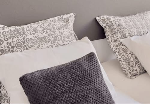 Bed with patterned pillows and gray waffle throw at Charm Discovery Experiences in Leiria