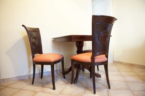 Elegante sala da pranzo a Residence La Corte con sedie in legno intagliato con cuscini arancioni e tavolo rotondo su base centrale