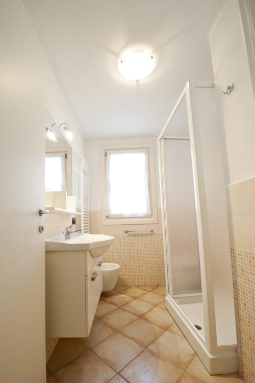 Bagno moderno e luminoso nell'appartamento Residence La Corte con lavandino bianco, wc, box doccia e pavimenti in piastrelle beige