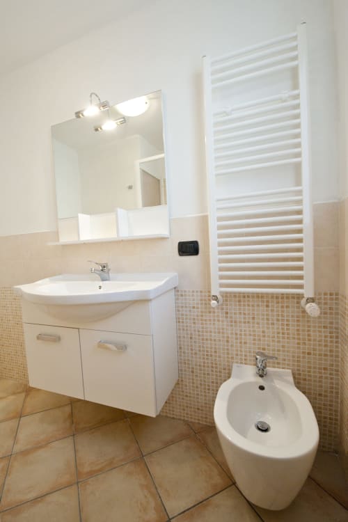 Bagno moderno con lavabo bianco, bidet, scaldarifiuti riscaldato e dettagli in mosaico presso Residence La Corte