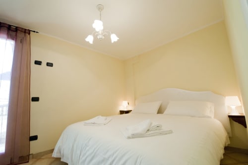 Camera luminosa in giallo brillante alla Residence La Corte di Vezza d'Oglio con letto bianco, lampade comodino e lampadario a sospensione
