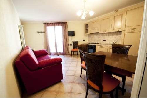 Luminoso appartamento a Residence La Corte con divano rosso, tavolo da pranzo, cucina attrezzata e accesso al balcone a Vezza d'Oglio
