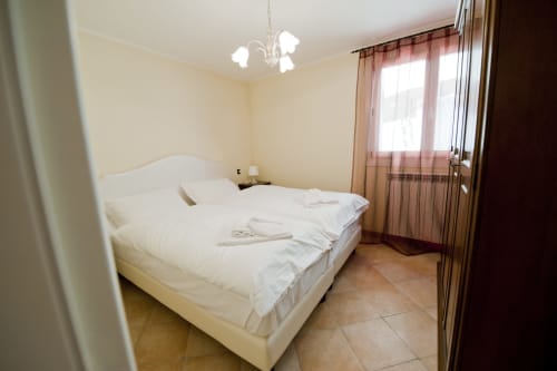 Camera luminosa con letto bianco, lampadario e finestre presso Residence La Corte a Vezza d'Oglio