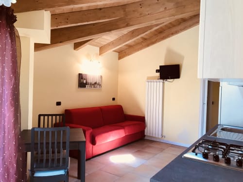 Monolocale a Residence La Corte a Vezza d'Oglio con divano rosso, travi in legno a vista, TV e angolo cottura