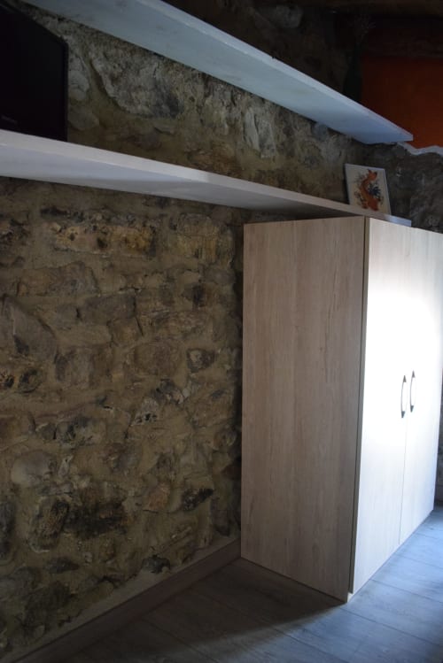 Habitación moderna en el albergue La Calma De Bellver con muro de piedra vista, estanterías blancas y armario de madera en Bellver de la