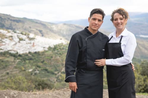 Dos chefs con uniformes profesionales en blanco y negro en El Paraje del Chef de Laroles, Granada, con vistas del paisaje montañoso