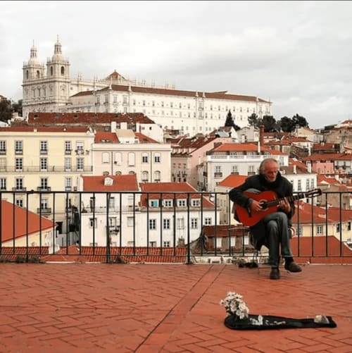 Músico tocando violão na varanda do telhado com vista para a histórica Leiria, Portugal, com a catedral ao fundo