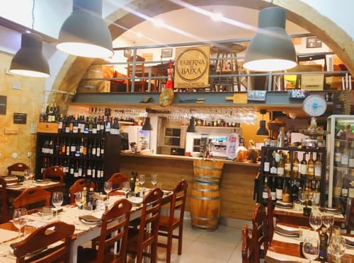 Taberna Baixa restaurant dining room in Leiria with wooden tables, wine shelves, and pendant lighting.