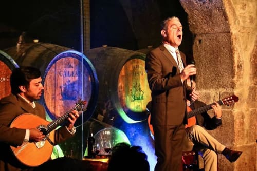Dois músicos se apresentam com guitarras na Charm Discovery Experiences em Leiria, Portugal, com barris de vinho iluminados