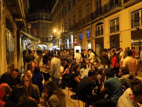 Cena noturna animada nas ruas de Leiria com multidões desfrutando da atmosfera vibrante ao redor da arquitetura histórica amarela