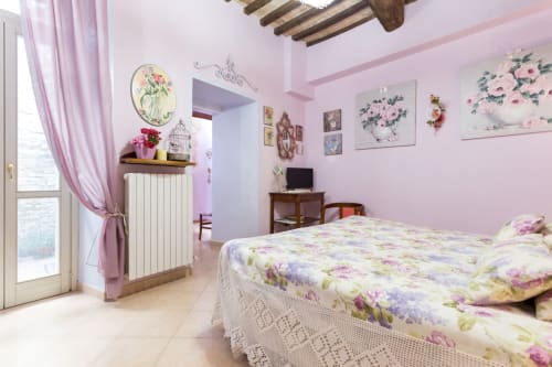 Camera rosa presso Dormire Assisi B&B con biancheria floreale, vista giardino e soffitto con travi rustiche