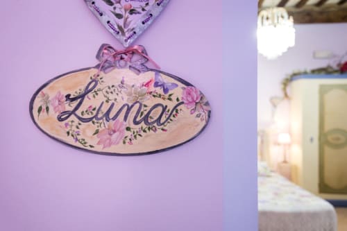 Insegna ovale decorativa con testo 'Lumina' e design floreale in viola e rosa appesa a parete lavanda presso Dormire Assisi