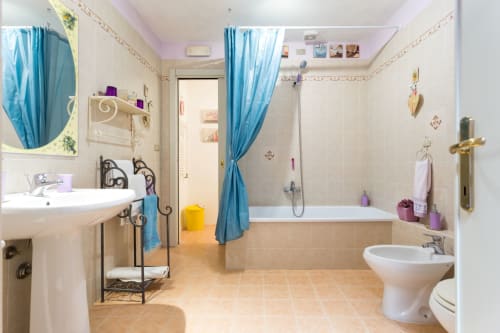Bagno spazioso a Dormire Assisi con vasca, doccia, doppio lavabo, dettagli blu e vista sul giardino