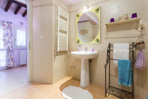 Bagno luminoso al Dormire Assisi B&B con lavabo su colonna, specchio ovale, scaldasalviette e accenti viola