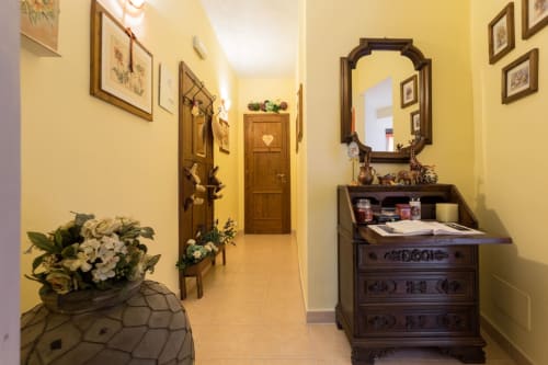 Elegante corridoio dell'Hotel Dormire Assisi con pareti gialle, porte in legno, opere d'arte incorniciate, mobili decorativi e fiori freschi