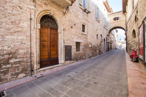 Storica via in pietra ad Assisi con porta ad arco e Vespa rossa vicino a Dormire Assisi B&B