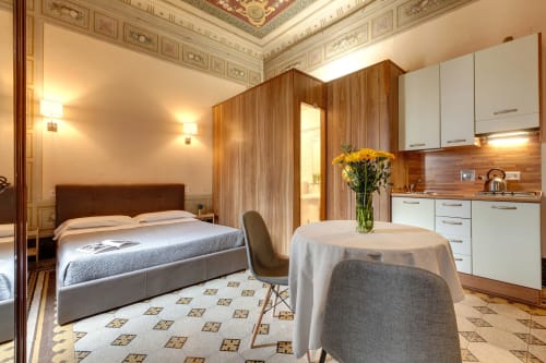 Camera da letto deluxe a Sleep tight Florence con divisorio in legno, cucina bianca, letto e soffitto ornato a Firenze