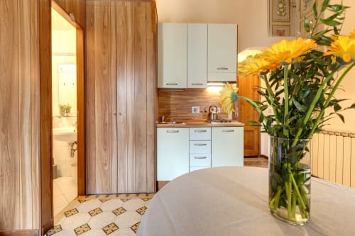 Elegante angolo cucina con mobili bianchi, rivestimento in legno e fiori gialli in B&B a Firenze