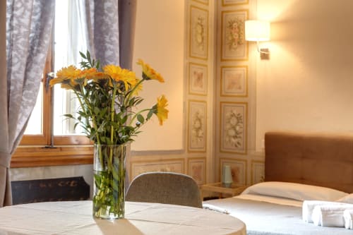 Camera d'hotel luminosa a Firenze con gerbere gialle in vaso di vetro, elegante guardaroba in legno e letto confortevole