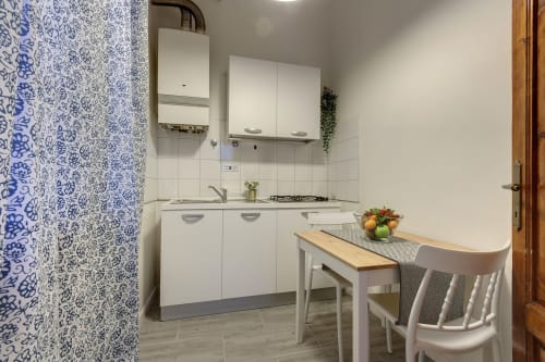Cucina moderna bianca con carta da parati a motivi blu, tavolo da pranzo e piano cottura a gas nell'appartamento Sleep Tight Florence a Firenze,