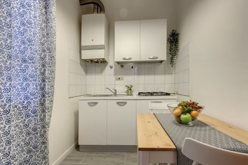 Modern kitchen in Florence apartment with white cabinets, gas hob, blue patterned door, wooden table and fresh fruit bowl