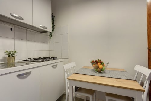 Modern kitchen and dining area in Florence apartment with white cabinetry, gas hob, and wooden table with fruit bowl