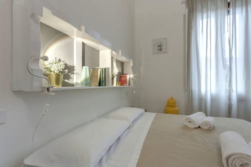 Modern bedroom with illuminated mirror shelf, white bedding, rolled towels, and natural light in Sleep Tight Florence