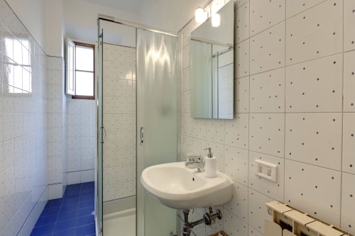 Modern bathroom with beige tiled walls, white sink, glass shower enclosure, and window at Sleep tight Florence apartment in