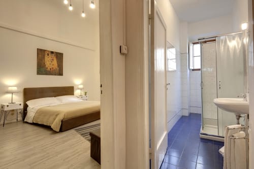 Modern bedroom with ensuite bathroom at Sleep Tight Florence BnB, featuring brown bed, pendant lights, and garden view