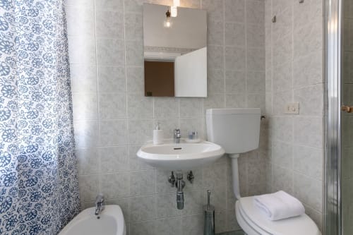 Modern bathroom in Sleep tight Florence apartment with round sink, mirror, toilet, and blue patterned shower curtain