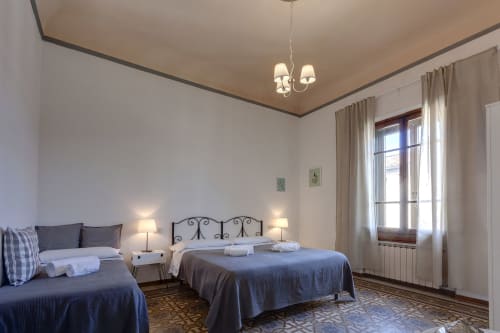 Spacious bedroom in Florence B&B with twin beds, elegant iron headboards, pendant lighting, and large windows with curtains