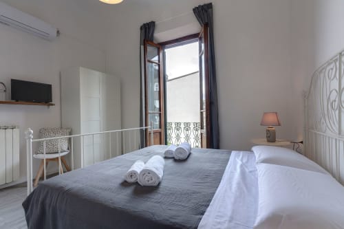 Bright Florence garden view apartment bedroom with white metal bed, dark curtains, balcony doors, TV, and modern amenities