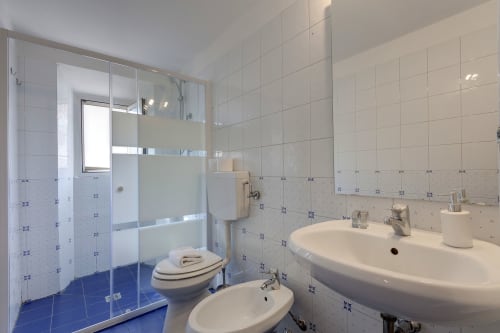 Modern bathroom with blue tile floor, dual sinks, glass shower enclosure, and toilet at Sleep tight Florence apartment in