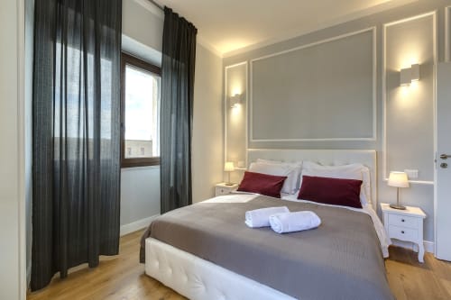Modern bedroom suite in Florence with city view, white headboard, burgundy pillows, dark curtains, and contemporary lighting
