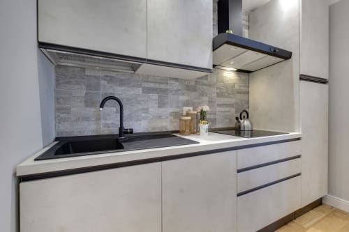 Modern kitchen in Sleep tight Florence suite with white cabinetry, black sink, gray tile backsplash, and stainless steel