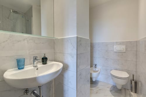 Modern bathroom in Florence hotel suite with curved white sink, marble tiles, toilet, bidet, and glass shower enclosure