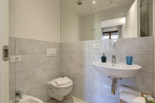 Bagno moderno in marmo presso Sleep tight Florence con wc sospeso, lavabo bianco curvo e finiture contemporanee