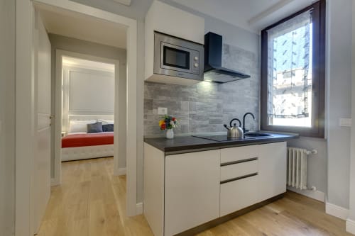 Moderno cucinotto in suite fiorentina con armadiatura bianca, piano di lavoro scuro e vista della camera da letto