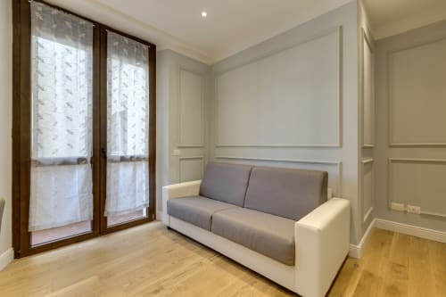 Suite moderna presso Sleep tight Florence con divano grigio e bianco, porte in legno con tende trasparenti e legno chiaro
