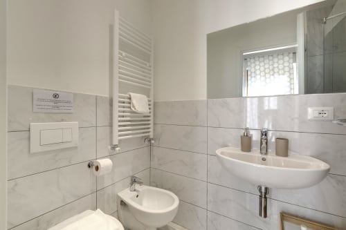 Modern bathroom at Sleep tight Florence B&B with marble tiles, wall-mounted sink, toilet, heated towel rack, and window