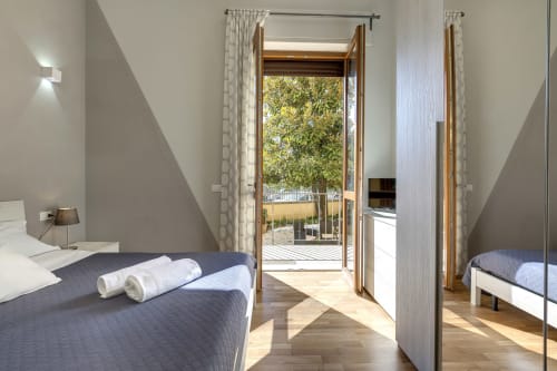 Modern bedroom at Sleep tight Florence with garden view, featuring bed, desk, and French doors opening to terrace with trees
