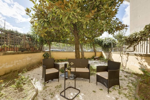 Garden seating area at Sleep tight Florence with wicker chairs under mature tree, yellow walls, and climbing vines