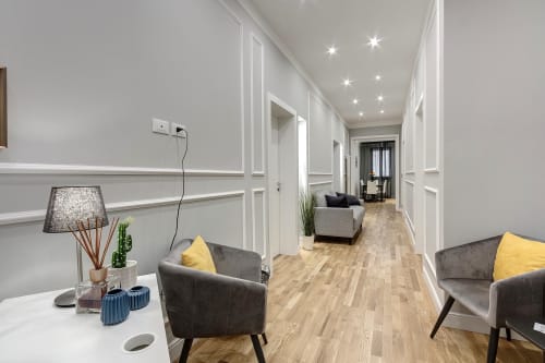 Modern hallway at Sleep tight Florence BnB with gray chairs, yellow cushions, wooden flooring, and ambient ceiling lights