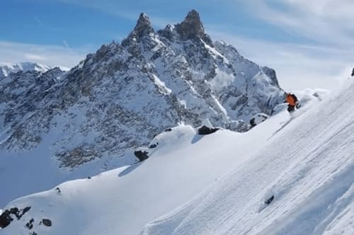 Pente enneigée près de CMD Méribel Le Pralin aux Allues, France avec pics rocheux dramatiques et skieur en orange