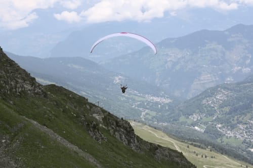 Parapentiste volant au-dessus de la vallée de Méribel avec les Alpes et les pentes verdoyantes des Allues, France